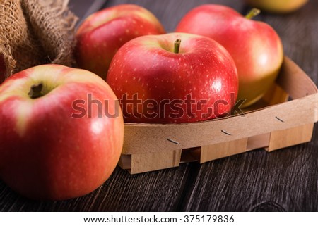 Closeup photo of tasty ripe juicy smooth red yellow apples in small crate box with burlap on grey wooden table, horizontal picture 
