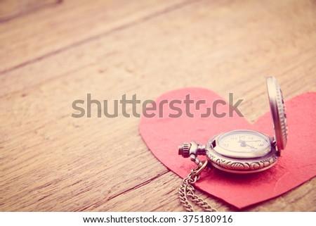 Long necklace antique style pocket watch with a red mulberry paper heart on a wooden surface. A symbol to express someone eternal love on special occasions i.e. Valentines day, Fathers & Mothers Day.