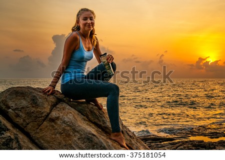 Young smiling woman sitting on the rocks by the sea and watching the sunrise on a tropical island Koh Samui, Thailand