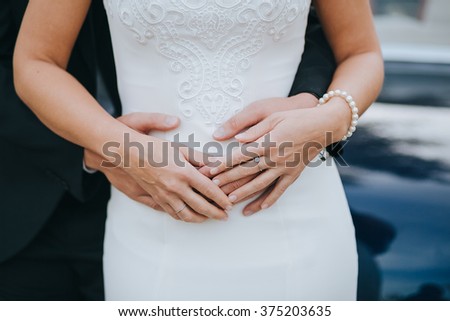 Wedding. The groom in a suit hugs bride in a white dress on a background of blue cars. In the hands of the bride's jewels