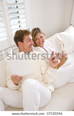 Couple relaxing together reading at home in white surroundings