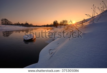Picture of a calling sun above the snow-bound bank of the not frozen river with an island on her