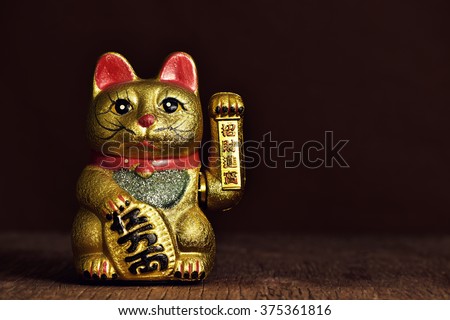 a golden chinese lucky cat with its left paw raised, on a rustic wooden surface Royalty-Free Stock Photo #375361816