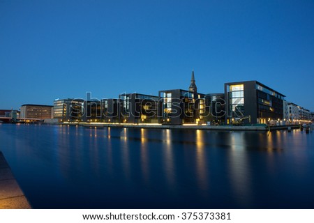 Reflection of Copenhagen in waterfront, showing a medieval church tower peeping out behind some new modern buildings at night Copenhagen bay view. Modern Copenhagen at night. Night Copenhagen seafront