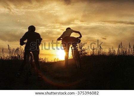summer landscape silhouette of a boy on a bicycle, with rolling hills on the background of golden sunset 