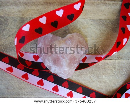 Pink gemstone in heart shape on wood background with ribbon