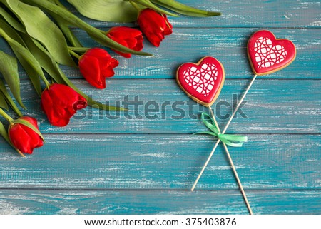 bouquet of red tulips lying on a white textured table next to the envelope and two handmade hearts
