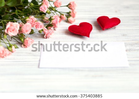 bouquet of small pink roses lying on a white textured table next to the envelope and two handmade hearts