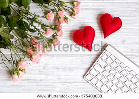 two handmade hearts lying on a white textural table next to a bouquet of pink  small roses and keyboard
