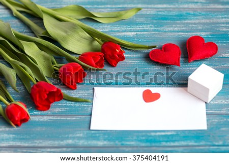 bouquet of red tulips lying on a blue textured table next to the envelope and two handmade hearts
