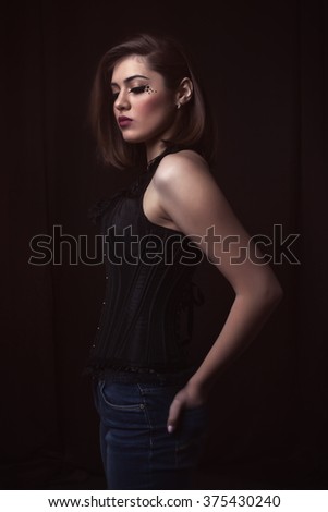 portrait of a beautiful girl in a corset on a dark background. make-up with the stars