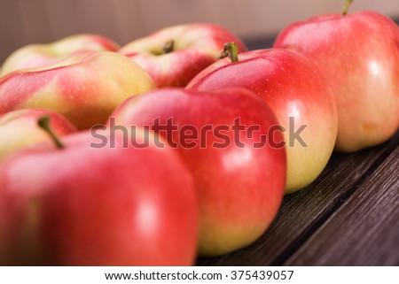Closeup photo of many ripe smooth sweet red yellow apples with stems lies side by side on grey wooden table, horizontal picture