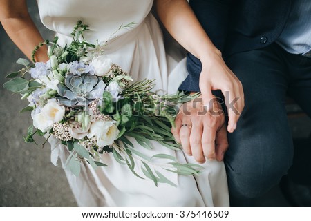 Wedding. The girl in a white dress and a guy in a suit sitting on a wooden chair, and are holding a beautiful bouquet of white, blue, pink flowers and greenery, decorated with silk ribbon Royalty-Free Stock Photo #375446509