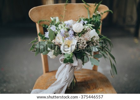 Bridal bouquet. The bride's bouquet. Beautiful bouquet of white, blue, pink flowers and greenery, decorated with long silk ribbon, lies on vintage wooden chair