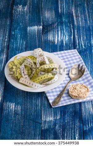 Measuring tape like spaghetti with crispy bread on white plate with fork on chequers napkin on blue wooden retro background