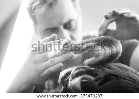 Professional hairdresser is styling curly hair. Emotional detail of the hands making hot styling in hair salon or photo studio for fashion shot. Black and white photography. Blurred background.