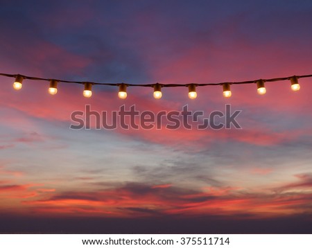 light bulbs on string wire against sunset sky Royalty-Free Stock Photo #375511714