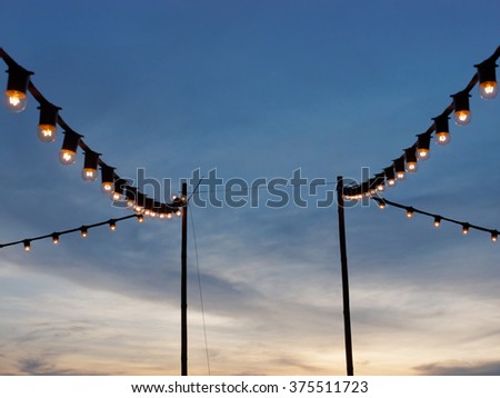 light bulbs on string wire hanging on poles against sunset sky Royalty-Free Stock Photo #375511723
