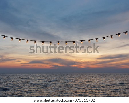 light bulbs on string wire against sunset sky by the beach Royalty-Free Stock Photo #375511732