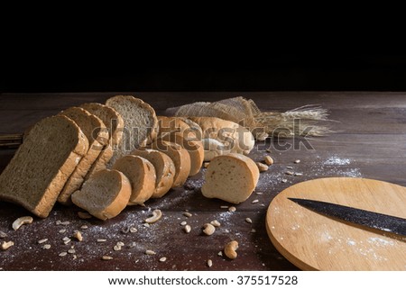 still life with bread, wheat, knife and wooden cutting board on wooden table