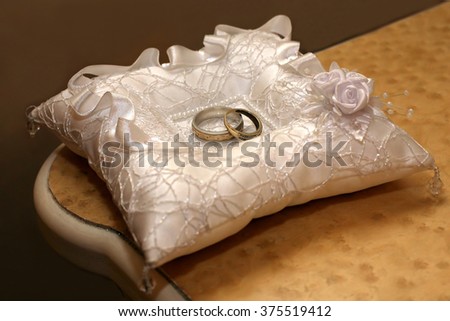 gold wedding rings lie on a decorative pillow
