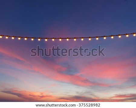light bulbs on string wire against sunset sky  Royalty-Free Stock Photo #375528982