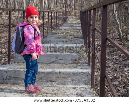 Little girl with a backpack going up the stairs. Road in a forest.