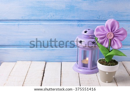 Decorative flower in pot and candle in lantern on  blue wooden background. Selective focus. Place for text.
