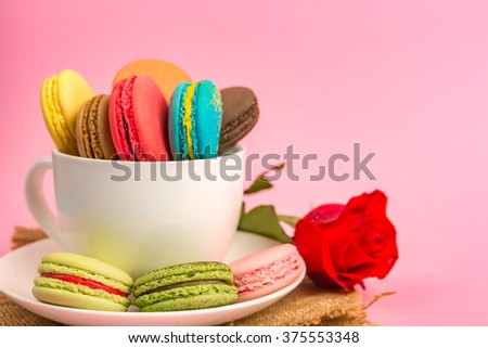 Side View and Selective Focus : Macaroons in Tea Cup with blur rose on pink background
