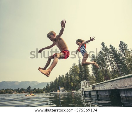 Kids jumping off the dock into a beautiful mountain lake. Having fun on a summer vacation at the lake with friends Royalty-Free Stock Photo #375569194