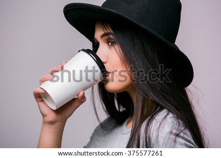 Portrait Woman in black hat with cup of hot drink - isolated on grey background. Series of poses.