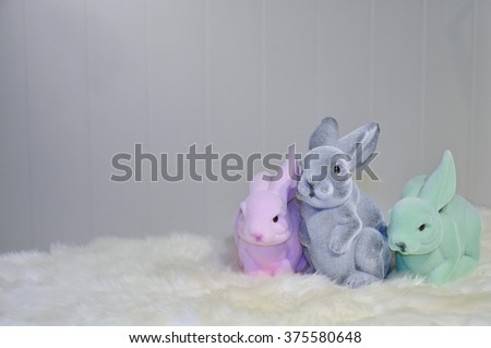 Facing view of three different colored easter bunnies on a white fur surface, in front of a light grey background