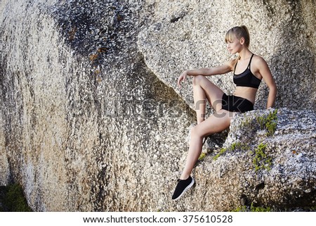 Gorgeous athlete sitting on rock, looking away
