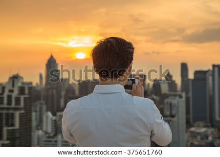 Man taking a photo of cityscape and sunset view with smartphone.