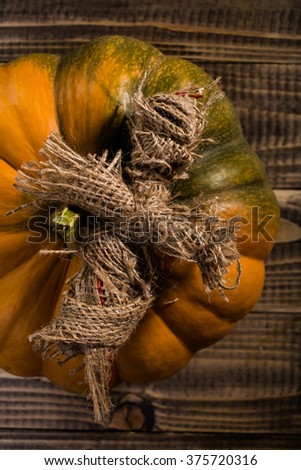 Top view of scary cross shaped Halloween magic burlap puppet on big orange segmented cucurbita with green spot on wooden table, vertical picture