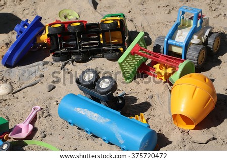 Many multicolored red blue green yellow boyish childish vehicle toys summer playful game in sandbox closeup outdoor on sand background, horizontal picture