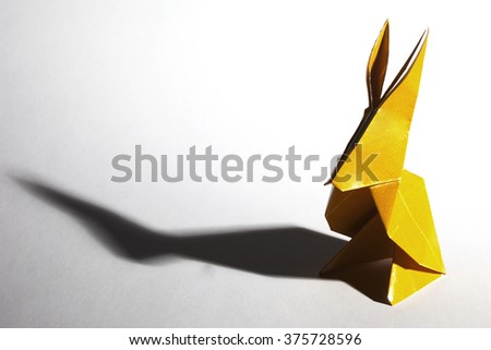 Yellow origami paper rabbit isolated on white background with long shadow.