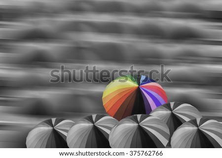 Multicolor umbrella on non-color group of umbrella with motion blurred background, concept to different idea