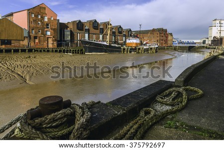 Hull, Humberside, UK. River Hull at low tide and an obsolete ship aground in the mud bank flanked by office and other buildings on one side and a barge anchored in the foreground, Hull, Yorkshire, UK. Royalty-Free Stock Photo #375792697