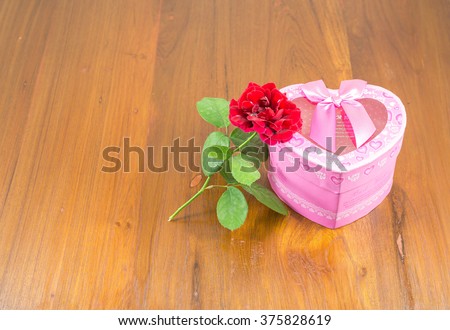 Heart-shaped Valentines Day gift box with rose over a wood background

