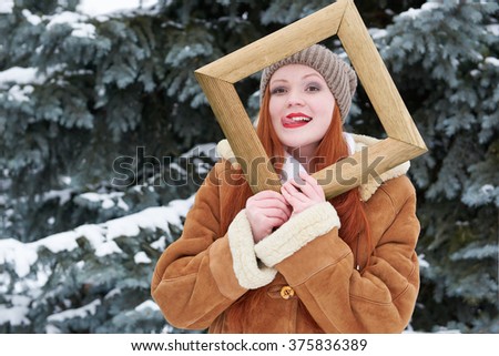 Woman portrait in wooden photo frame at winter season. Snowy weather in fir tree forest.
