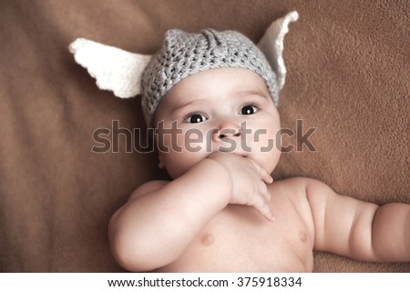 Cute baby boy lie  on a beige background wearing a crochet viking hat