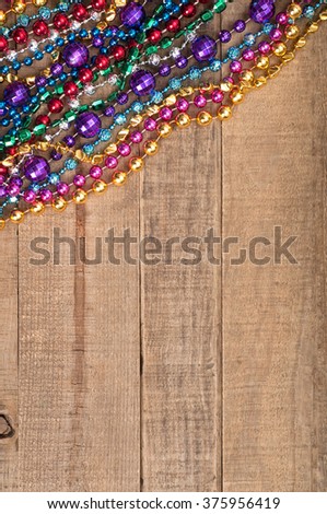  Festive Top View of Bright and Colorful Mardi Gras Bead Strands in upper corner on Rustic Brown, Textured Board Plank Background with Blank Space or Room for copy, text, your words.  Vertical 