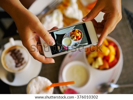 Hands with the phone close-up pictures of food. Breakfast for two : yogurt, coffee, fruit , toast. Royalty-Free Stock Photo #376010302