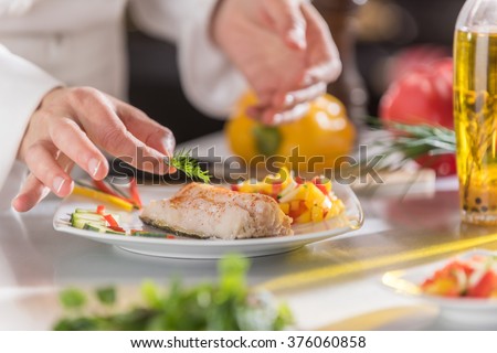 closeup on the hands of a chef in a professional kitchen carefully depositing a sprig of dill on a cod fillet Royalty-Free Stock Photo #376060858