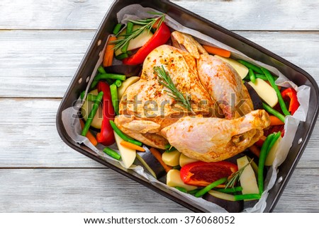 raw whole chicken with colorful pieces of peppers, potatoes. eggplant, green beans rosemary leaves in the baking dish, preparing for roast in the oven, top view, close-up 