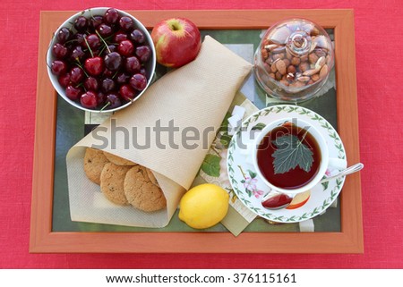 Still life with tea, homemade oatmeal cookies with raisins, cherries, lemon, apple, nuts and lump sugar on a wooden tray. Breakfast or tea-break.