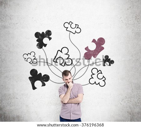 A man standing with a hand on his chin at a concrete wall with parts of a puzzle drawn on it. Front view. Concept of getting a full picture.