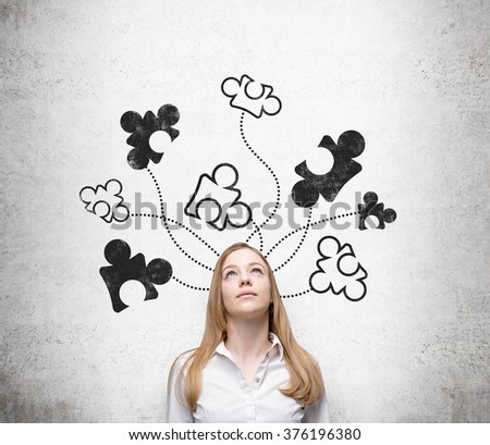 A beautiful young woman standing at a concrete wall with parts of a puzzle drawn on it, looking up. Front view. Concept of getting a full picture.