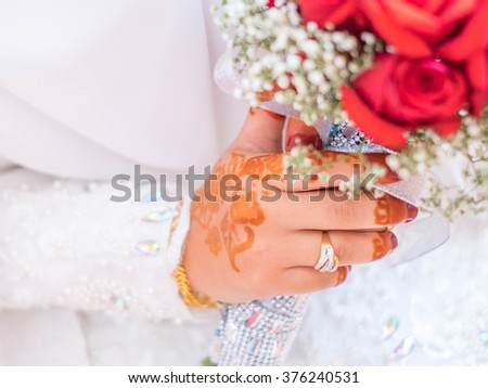 Beautiful bride hand with details of wedding ring and henna. She was holding a bouquet of red roses with out of focus bokeh effect.  